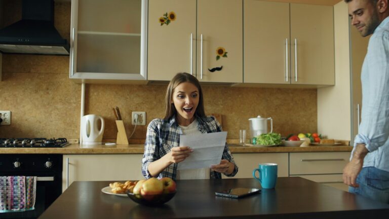 Parents review insurance documents beside a newborn at a kitchen table.