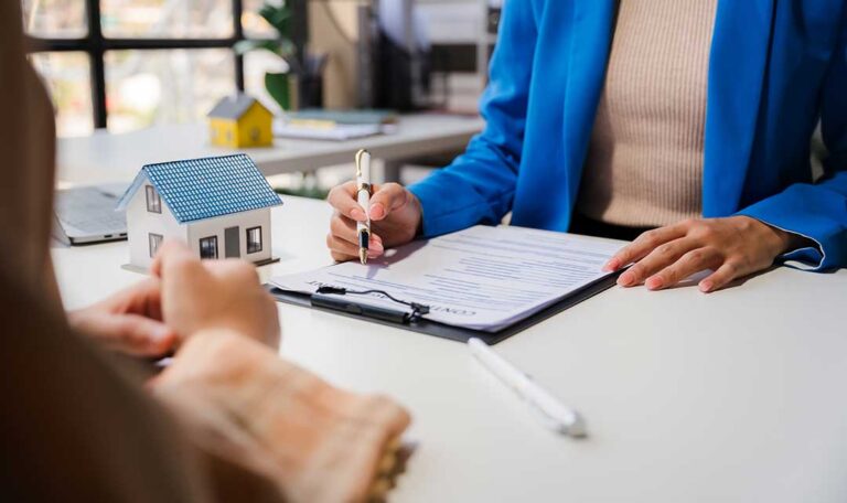 Two people compare property damage photos, repair estimates, and an insurance policy at a table.